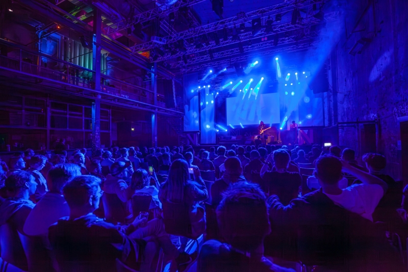 Blick über einen in blaues Licht getauchten Zuschauerraum auf eine Bühne mit Musikern